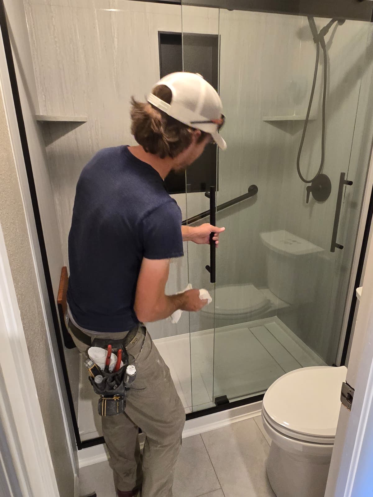 Installer finishing a newly installed glass shower door in a remodeled bathroom
